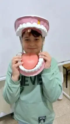 Qassem, de ojos marrones, el pelo peinado y una sudadera verde, sonríe a la cámara a través de una réplica gigante de dientes, encías y lengua, en su colegio, en el Líbano.
