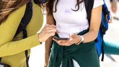 Duas jovens com mochilas olham para o telefone celular