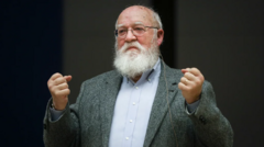 Daniel Dennett fazendo gestos com as mãos, com os punhos fechados e erguidos para cima; ele tem olhar confiante