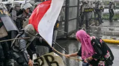 Seorang demonstran perempuan memukul petugas polisi dengan tongkat bambu yang diikatkan bendera Indonesia saat aksi demo 28 Agustus 2025.