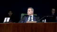 André Mendonça, sentado, durante julgamento no Plenário da Primeira Turma do STF. Atrás dele, em segundo plano, duas pessoas acompanham sentadas, com olhar para baixo. 