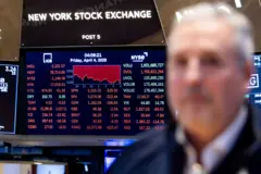 Operador do mercado financeiroa desfocado em frente a painel que exibe queda das ações negociadas na Bolsa de Nova York