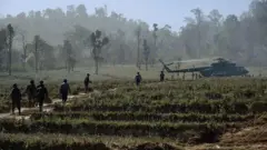 စစ်ရဟတ်ယာဥ်တစ်စင်းဆီ သွားနေတဲ့ မြန်မာစစ်တပ်တပ်ဖွဲ့ဝင်တွေ။ တောင်ပေါ်ဒေသမှာဖြစ်ပြီး လယ်ကွက်တစ်ခုကို ဖြတ်သွားနေတာဖြစ်ပါတယ်။