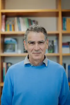 Foto de Fernando Limongi usando camisa azul em frente a prateleira de livros