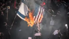Iranian protesters burn an Israel and the US flags while attending a mass funeral for the commander Qasem Soleimani,