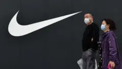 Two people walk in front of the Nike logo of the Nike flagship store at Wangfujing Pedestrian Street in Beijing, China.