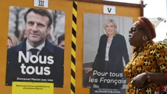 A woman walks past posters of Macron and Le Pen