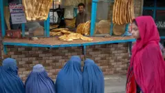 কাবুলে এক রুটির দোকানের সামনে রুটির অপেক্ষায় তিন আফগান নারী। বহু মানুষ এখন খাদ্য সংকটে আছে।