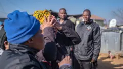 A relative of one of the victims shot dead in a tavern in Soweto reacts next to the crime scene in Soweto