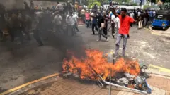 A Sri Lankan pro government protester celebrates after setting anti-government protester's tents on fire as police officers look on infront of temple trees
