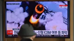 People watch a television screen showing a news broadcast with file footage of a North Korean missile test, at a railway station in Seoul on March 16, 2022