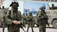 Armed servicemen wait near Russian army vehicles outside a Ukrainian border guard post in the Crimean town of Balaclava, March 1, 2014.