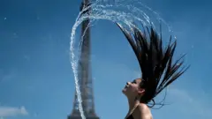 A woman plays the water as she cool herself down in the fountain of the Trocadero esplanade in Paris on June 25, 2019