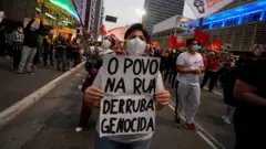 Manifestante segura cartaz onde se lê 'o povo na rua derruba genocida'