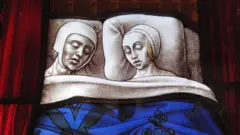 Vidriera medieval de una iglesia que muestra a una pareja del Medievo durmiendo