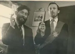 Dois homens vestindo ternos e gravatas e sorrindo para a câmera