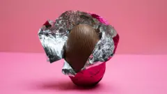 Um ovo de páscoa com embalagem aberta em fundo rosa