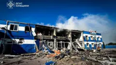 Двухэтажное здание завода, частично разрушенное в результате удара.