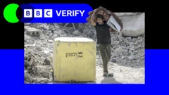 Katlanmış bir yatak taşıyan bir adam, Gazze'de İsrail ordusu tarafından koyulan sarı hattın yanından geçiyor. Arka planda molozlar var. Fotoğraf, BBC Verify logosu ve renklerinin üzerine yerleştirilmiş.