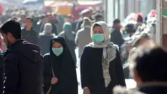 دو زن درحالیکه ماسک به صورت دارند در هوای الوده در کابل قدم میزنند.