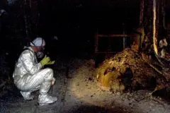 Pesquisador agachado tirando foto da 'pata de elefante', uma formação de cório sob o reator 4 de Chernobyl