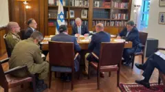 Minisitiri w'intebe wa Israel Benjamin Netanyahu, yafotowe mu kiganiro na Perezida Biden. Yicaye imbere y'ameza yo mu giti, akikijwe n'abajyanama barindwi, ibendera rya Israel riraboneka inyuma ye. 