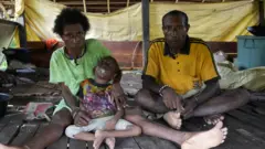 Keluarga Maurenus Merne tinggal di Kampung Anggreso, Kabupaten Mamberamo Raya. Anak bungsunya, Petra, lumpuh sejak balita dugaannya selama mengandung, mama Ester tidak mendapatkan asupan makanan bergizi dan vitamin yang memadai.