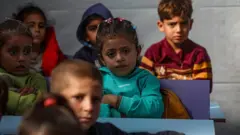 Niños pequeños sentados en una escuela temporal en una tienda de campaña.