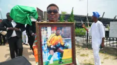 Aworan ọmọbinrin Peter Rufai to gbe aworan oloogbe naa lọwọ ni iboji rẹ to wa ni Ikoyi, niluu Eko