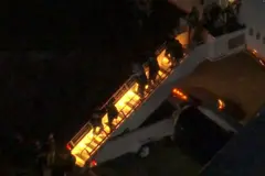 Varias personas, entre las que se supone que está Maduro, bajan del avión por una escalera iluminada, rodeados de agentes de seguridad, en un entorno sin luz, ya de noche.