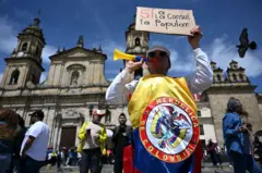 Homem com bandeira da Colômbia e um cartaz que diz "sim à consulta popular"