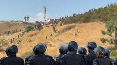 Moroccan security forces monitor dozens of migrants who have gathered on the outskirts of the border town of Castillejos, Morocco