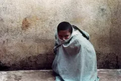 Paciente agachado e encolhido perto de muro, envolto em uma roupa