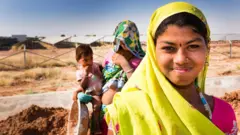 બીબીસી ગુજરાતી, બીબીસી, અમદાવાદ, ગુજરાત, યુપીએ, એનડીએ, ભાજપ, મનરેગા, એક, 2005માં સંસદમાં રાષ્ટ્રીય ગ્રામીણ રોજગાર ખાતરી અધિનિયમ નામે કાયદો પસાર થયો અને એ યોજના 'નરેગા' તરીકે ઓળખાઈ. ટૂંક સમયમાં જ એ યોજના મહાત્મા ગાંધી નૅશનલ રૂરલ ઍમ્પ્લૉયમેન્ટ ગૅરંટી ઍક્ટ (MGNREGA – મનરેગા) તરીકે ઓળખાઈ.
2025 એટલે, 20 વરસ બાદ, સંસદમાં કાયદામાં સુધારો કરી નવા નામ સાથે અવતરી છે.
આ યોજનાનું બિલ સંસદમાં 'વિકસિત ભારત – ગૅરંટી ફૉર રોજગાર ઍન્ડ આજીવિકા મિશન (ગ્રામીણ)' નામે મુકાયું અને પસાર થયું. હવે એને જી – રામ – જી તરીકે પ્રચલિત કરવામાં આવી રહ્યું છે. (રાષ્ટ્રપતિ દ્રૌપદી મુર્મૂએ તેને મંજૂરી પણ આપી દીધી છે.)
