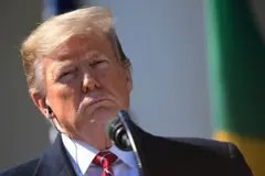 Donald Trump diante de microfone em foto de 2019 — a bandeira do Brasil aparece fora de foco no canto direito