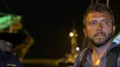 Thiago Ávila olhando para o lado durante a noite, em área portuária