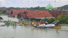 Warga naik perahu di depan rumah yang terendam banjir di Desa Ketanjung, Karanganyar, Demak, Jawa Tengah, Minggu (17/3/2024)