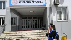 Saldırı olan okulun merdivenlerinde karanfiller ve önünden ağlayarak geçen bir kadın