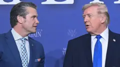 Слева министр обороны США Пит Хегсет, справа президент Дональд Трамп, они сфотографированы в момент обмена репликами. Хегсет выделяется платком в виде американского флага в нагрудном кармане пиджака