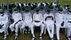 Mutane sanya da farin kaya da koriyar hula zaune a kujera