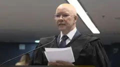 Demóstenes segurando papéis e falando ao microfone em sala de audiência