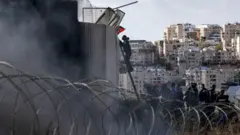 Bir gösterici, işgal altındaki Batı Şeria'da İsrail'in kurduğu bariyerin tepesindeki dikenli tellere Filistin bayrağını sabitliyor