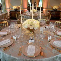 Una mesa de banquete redonda dispuesta para el servicio de cena con un arreglo floral redondo de rosas blancas en el centro de la mesa.