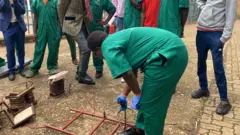 Umukobwa urimo gukanika akikijwe n'abandi bigana n'umwarimu