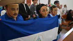 Nicaragüenses en el exilio con el rostro cubierto, sosteniendo una bandera nicaragüense, asisten a misa en la Iglesia de San Francisco en San José, Costa Rica, el 19 de abril de 2026. El servicio conmemora el aniversario del levantamiento social y político de 2018 en Nicaragua.