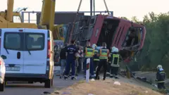 Dźwig podnosi przewrócony autobus. Na miejscu pracują strażacy i służby ratunkowe.