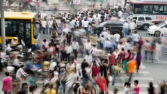 يتحوّل العدد الهائل من المشاة الذين يعبرون التقاطع المزدحم في منطقة التسوّق "سيدان" إلى كتلة ضبابية من الحركة مع حلول الغسق خلال عطلة عيد العمّال. ويُعدّ التسوّق أحد أكثر الأنشطة شيوعاً بين أبناء الطبقة الوسطى الجديدة في الصين.
