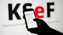 Strona internetowa Krajowego Systemu e-Faktur jest wyświetlana na ekranie telefonu komórkowego, a logo KSeF jest widoczne na ekranie komputera w Krakowie
