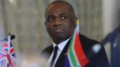 David Lammy yambaye  ikoti yirabura n'ikaruvati, ariko araraba  muri kamera