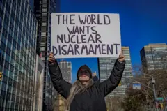 Um manifestante de jaqueta preta segura uma faixa que diz: "O mundo quer desarmamento nuclear".